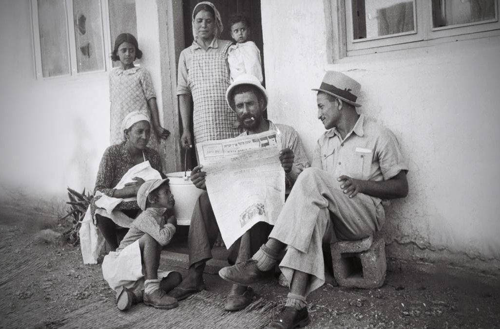 משפחה תימנית בפתח ביתה במושב אלישיב קוראת עיתון דבר (צילום: חנניה הרמן / לשכת העיתונות הממשלתית)