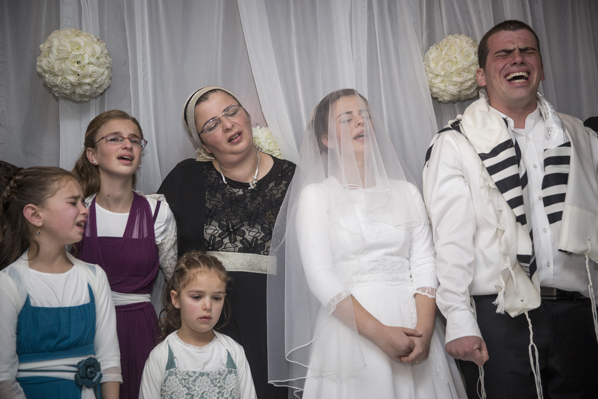 שרה ליטמן ואריאל ביגל מוקפים בבני משפחתם, במהלך חתונתם בירושלים. אביה ואחיה של שרה נרצחו שבועיים לפני כן בידי טרוריסטים פלסטינים (צילום: הדס פרוש / פלאש 90. באדיבות תערוכת עדות מקומית).