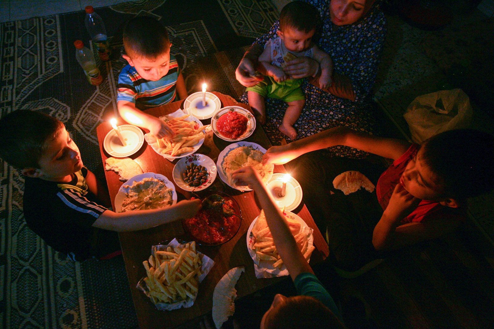 משפחה בעזה אוכלת ארוחה לאור נר עקב הספקת החשמל (צילום: עבד אל ראחים כ'תיב/ פלאש 90).