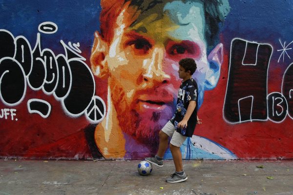 ילד משחק כדורגל על רקע גרפיטי של שחקן ברצלונה ליונל מסי (AP Photo/Manu Fernandez)