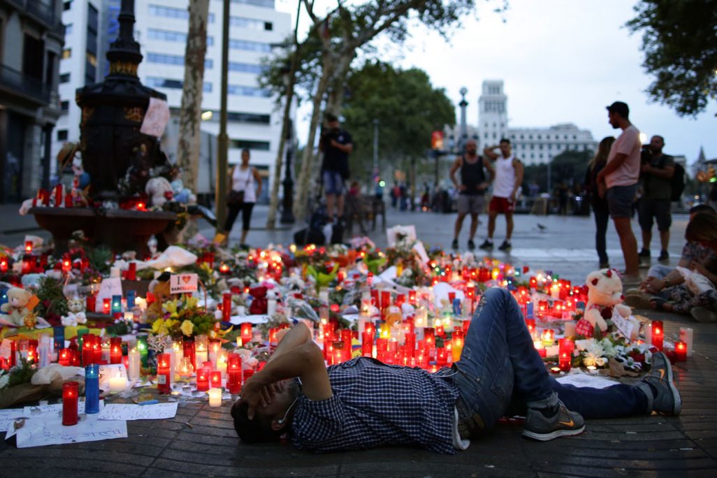 אנשים יושבים ליד נרות, פרחים, ומכתבים שהונחו בזירת הפיגוע בברצלונה (AP Photo/Manu Fernandez)