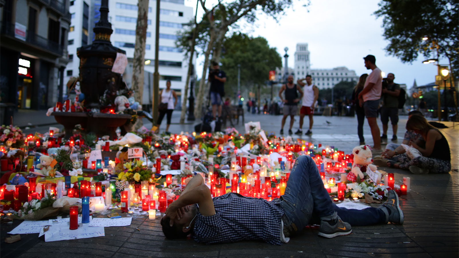 אנשים יושבים ליד נרות, פרחים, ומכתבים שהונחו בזירת הפיגוע בברצלונה (AP Photo/Manu Fernandez)