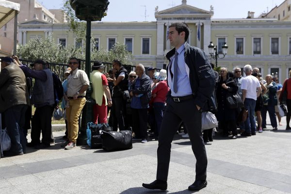 הולך רגל עובר ליד תור לחלוקת מזון באתונה. ברקע, בניין הבנק הלאומי של יוון (צילום: (AP Photo/Thanassis Stavrakis).
