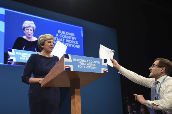 הקומיקאי סיימון ברודקין מגיש לראשת ממשלת בריטניה, תרזה מיי, טופס פיטורין בזמן שהיא נואמת על הבמה (צילום: (Joe Giddens/PA via AP).
