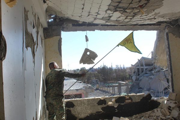 חייל מכוחות מ-SDF מנופף בדגל כורדי בבניין בעיר א-רקה לאחר קרב עם כוחות דאע"ש (צילום: Syrian Democratic Forces via AP)