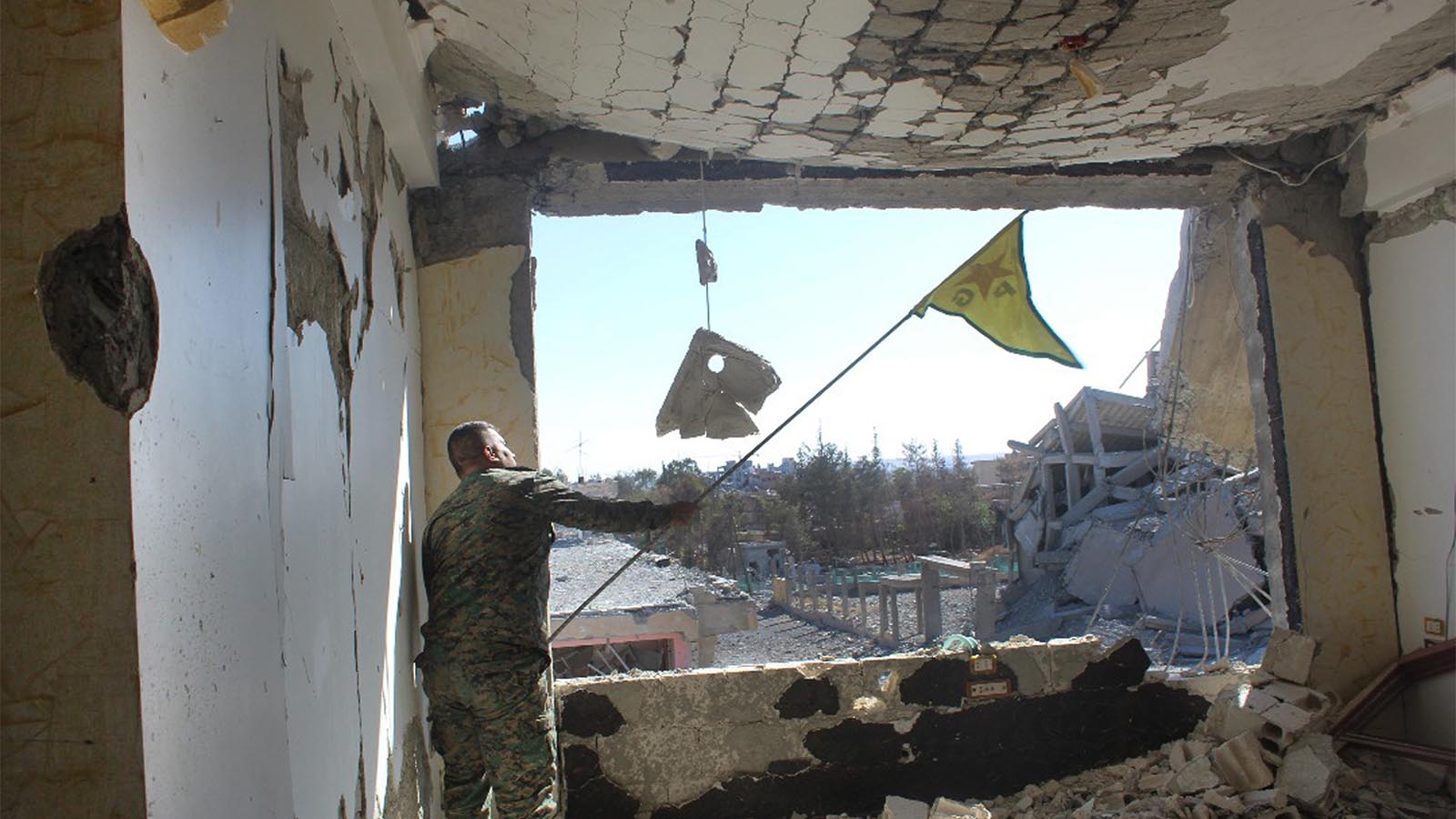 חייל מכוחות מ-SDF מנופף בדגל כורדי בבניין בעיר א-רקה לאחר קרב עם כוחות דאע&quot;ש (צילום: Syrian Democratic Forces via AP)