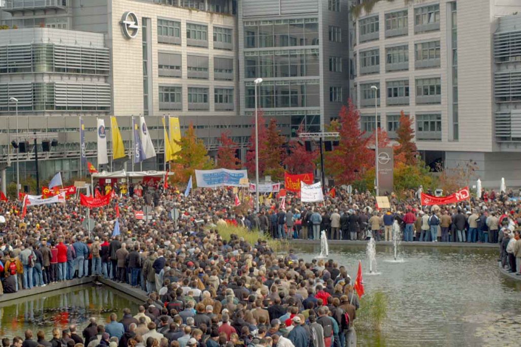 עובדי ג'נרל מוטורס בגרמניה מפגינים מול מפעלי החברה ב"יום פעולה כללי" במחאה על רצון החברה לפטר 12,000 מעובדיה באירופה. 19 באוקטובר 2004 (צילום: AP Photo/Bernd Kammerer)