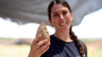 מעין שמר, מנהלת החפירה מטעם רשות העתיקות, מציגה אבן יד בת חצי מליון שנה (צילום: שמואל מגל / רשות העתיקות).