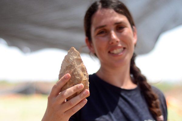 מעין שמר, מנהלת החפירה מטעם רשות העתיקות, מציגה אבן יד בת חצי מליון שנה (צילום: שמואל מגל / רשות העתיקות).