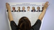 עובדת תולה בקלפי שלט עם רשימת המועמדים בבחירות לנשיאות רוסיה (AP Photo/Dmitri Lovetsky)