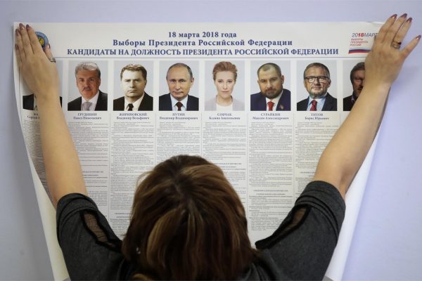 עובדת תולה בקלפי שלט עם רשימת המועמדים בבחירות לנשיאות רוסיה (AP Photo/Dmitri Lovetsky)