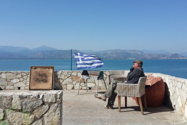 יווני זקן מביט לנוף כשברקע דגל יוון. צילום: רז רותם