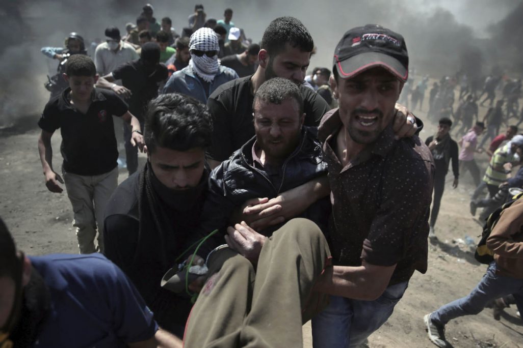 פלסטינים סוחבים פצוע בעקבות העימותים עם כוחות הביטחון בגבול רצועת עזה. 14 במאי (AP Photo/Khalil Hamra)