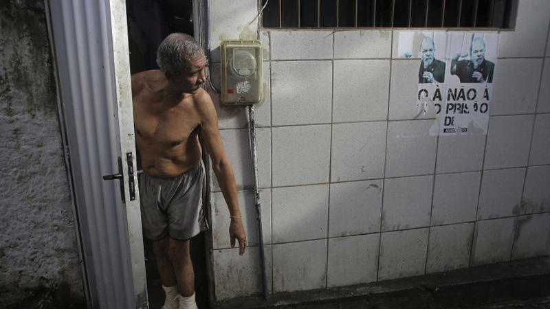 אדם עומד ליד שלטי תמיכה בלולה דה סילבה בביתו שבברזיליה טיימוסה (צילום: AP Photo/Eraldo Peres).
