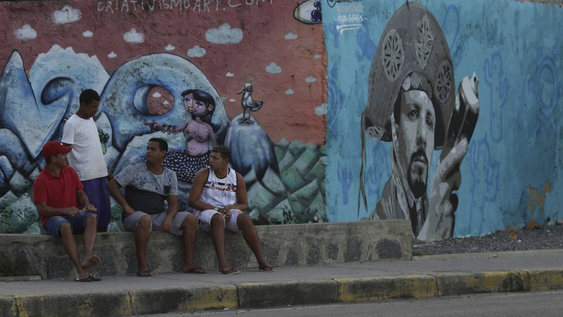 חבורת אנשים יושבים על מדרכה בטיימוסה שעברה מהפך אורבני בתקופתו של דה סילבה (צילום: AP Photo/Eraldo Peres).