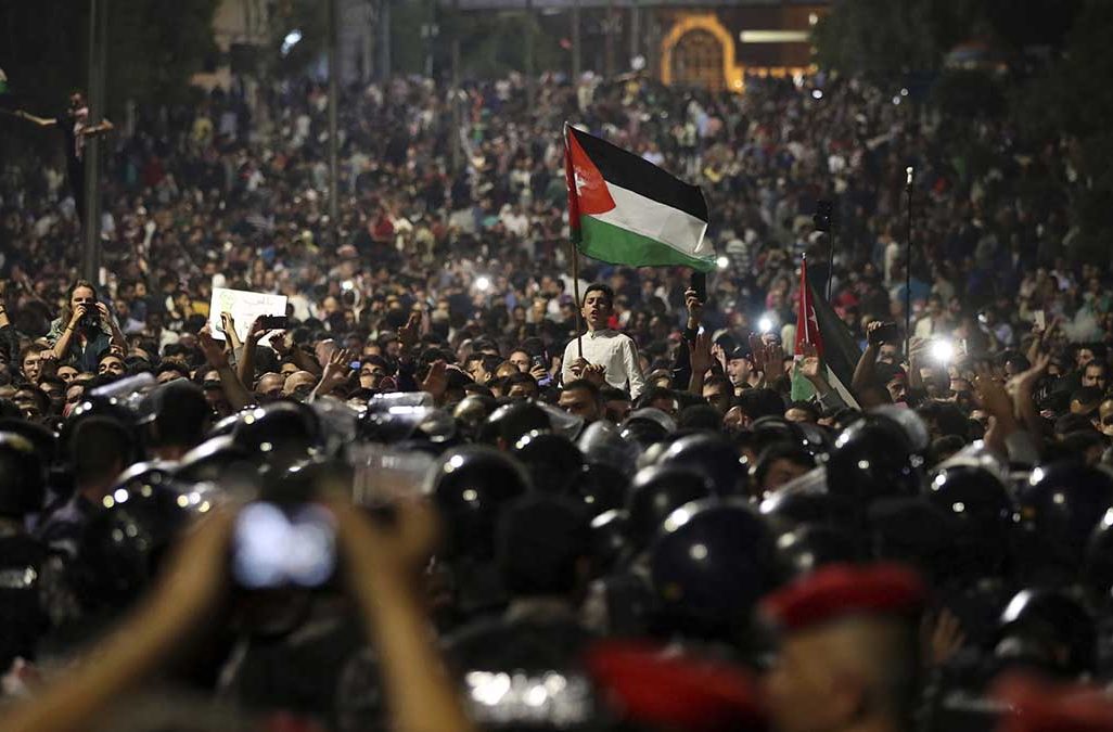 Jordanian protesters shout slogans and raise a national flag during a demonstration outside the Prime Minister's office in the capital Amman early Monday, June 4, 2018.  Thousands of Jordanians protested against a planned tax increase for a fourth straight day Sunday, marching toward the office of the prime minister and demanding his resignation. (AP Photo/Raad Adayleh)