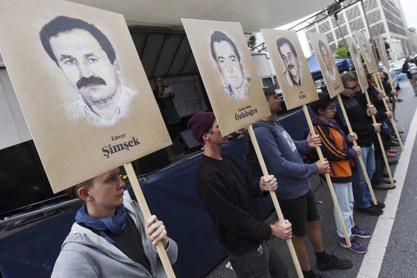 מפגינים אוחזים בשלטים עם תמונות הנרצחים מחוץ לבית המשפט במינכן לפני הקראת גזר הדין של חברי ארגון הטרור הנאו-נאצי. 11 ביולי 2018  (Tobias Hase/dpa via AP)