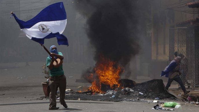 מפגין רעול פנים מנופף בדגל ניקרגואה ליד מחסום שהועלה באש, 12 במאי 2018. (צילום: AP Photo/Alfredo Zuniga)