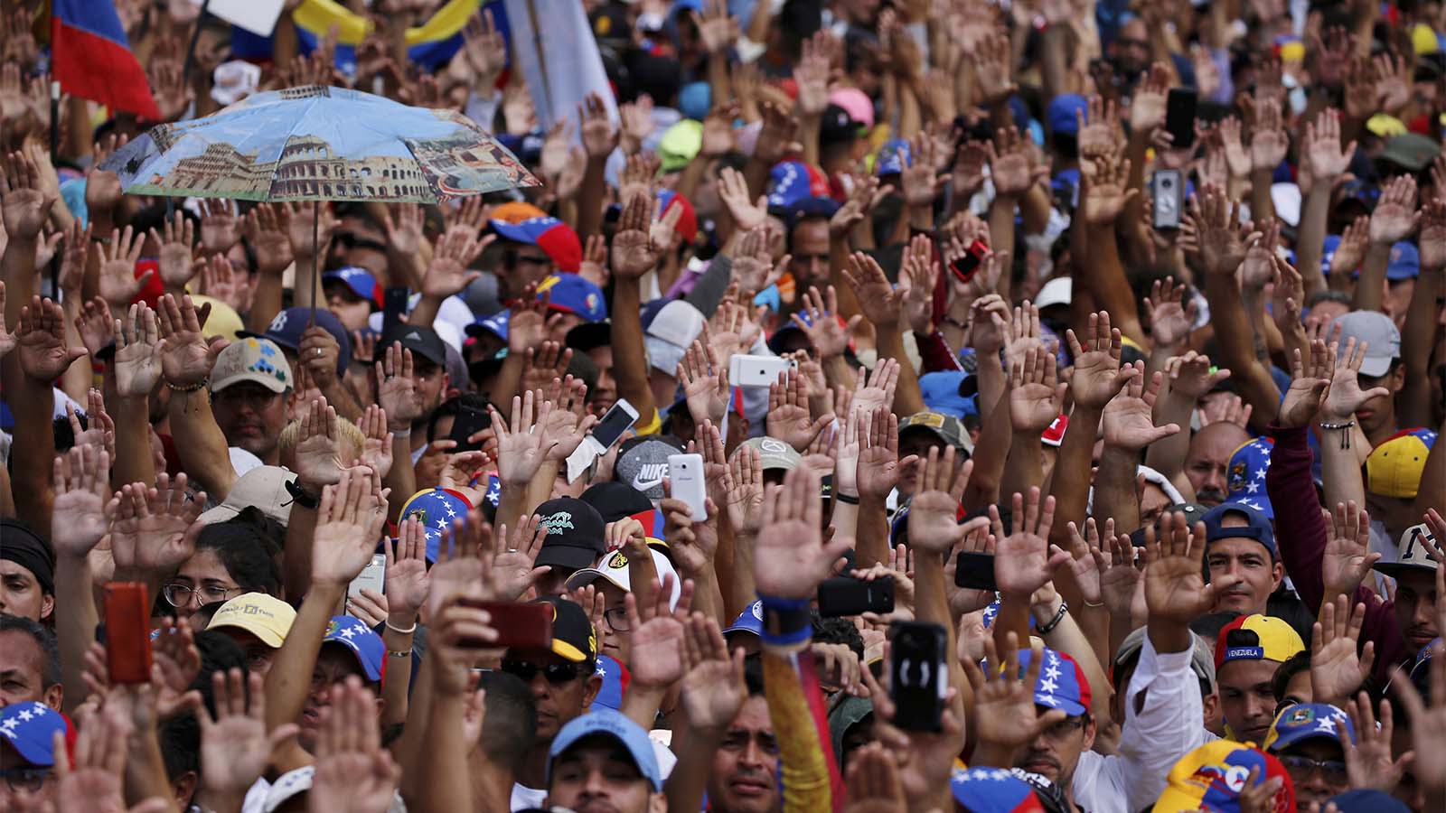 Anti-government protesters hold their hands up during the symbolic swearing-in of Juan Guaido, head of the opposition-run congress, who declared himself interim president of Venezuela, during a rally demanding President Nicolas Maduro's resignation in Caracas, Venezuela, Wednesday, Jan. 23, 2019. (AP Photo/Fernando Llano)