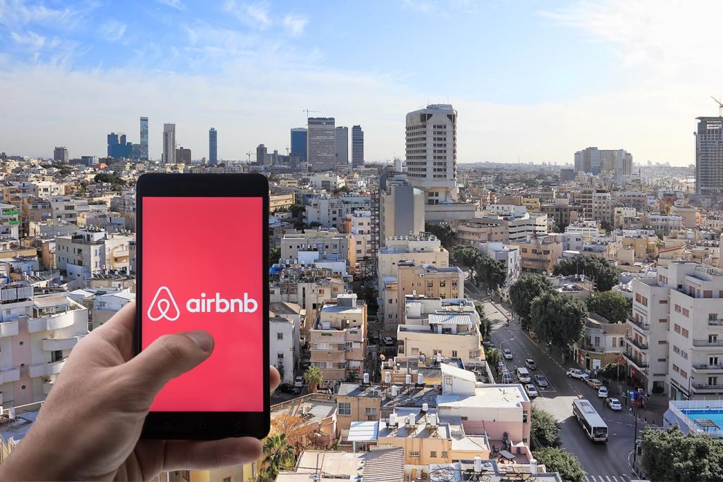 אפליקציית Airbnb ברקע העיר תל אביב (צילום: Shutterstock)