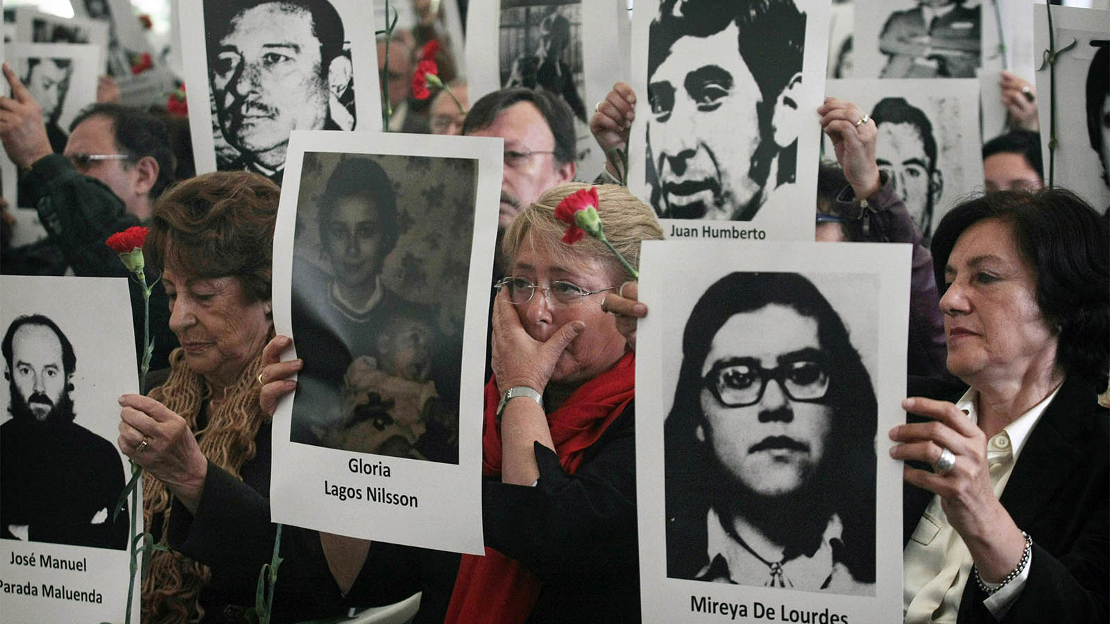 נשיאת צ'ילה, מישל בצ'לט, עומדת ב-2013 עם אמה וצ'יליאנים נוספים כשהן אוחזות תמונות של קורבנות משטרו של אוגוסטו פינושה, רודן צ'ילה (AP Photo/Luis Hidalgo, File)