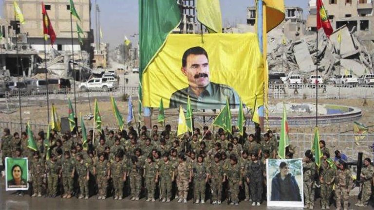תמונותו של עבדאללה אוג'לאן מנהיג ה-PKK במסדר צבאי של לוחמות כורדיות לאחר שניצחו את דאע"ש בא-ראקה, סוריה. 19 באוקטובר 2017 (Ronahi TV, via AP)