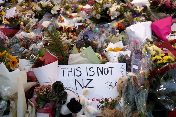 שלט "זאת לא ניו-זילנד" בין זרי הפרחים לזכר קורבנות הטבח (צילום: AP Photo/Vincent Yu).