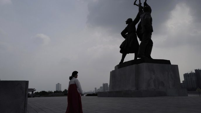 מדריכת תיירים צפון קוריאנית חולפת על פני פסל הניצב מחוץ למגדל אידאולוגיית הג'וצ'ה בפיונגיאנג. (צילום: AP Photo/Vincent Yu)
