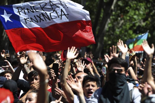 מפגינים צ'ילאנים מניפים דגל עליו כתוב "פיניירה, התפטר" במהלך מחאות ברחבי צ'ילה. 21 באוקטובר 2019 (AP Photo/Miguel Arenas)