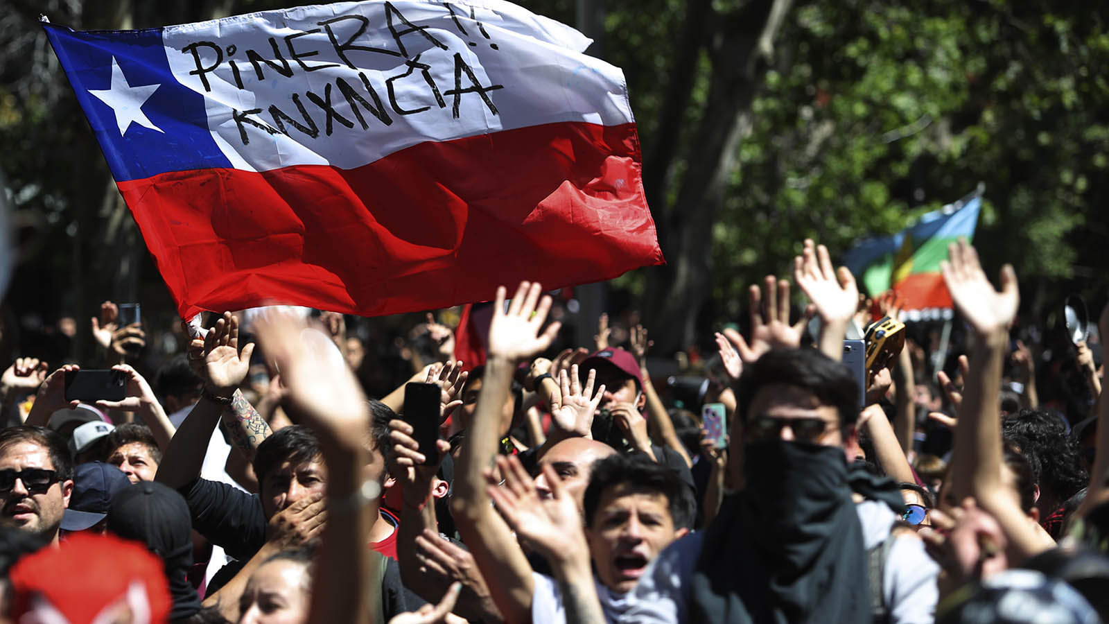 מפגינים צ'ילאנים מניפים דגל עליו כתוב &quot;פיניירה, התפטר&quot; במהלך מחאות ברחבי צ'ילה. 21 באוקטובר 2019 (AP Photo/Miguel Arenas)