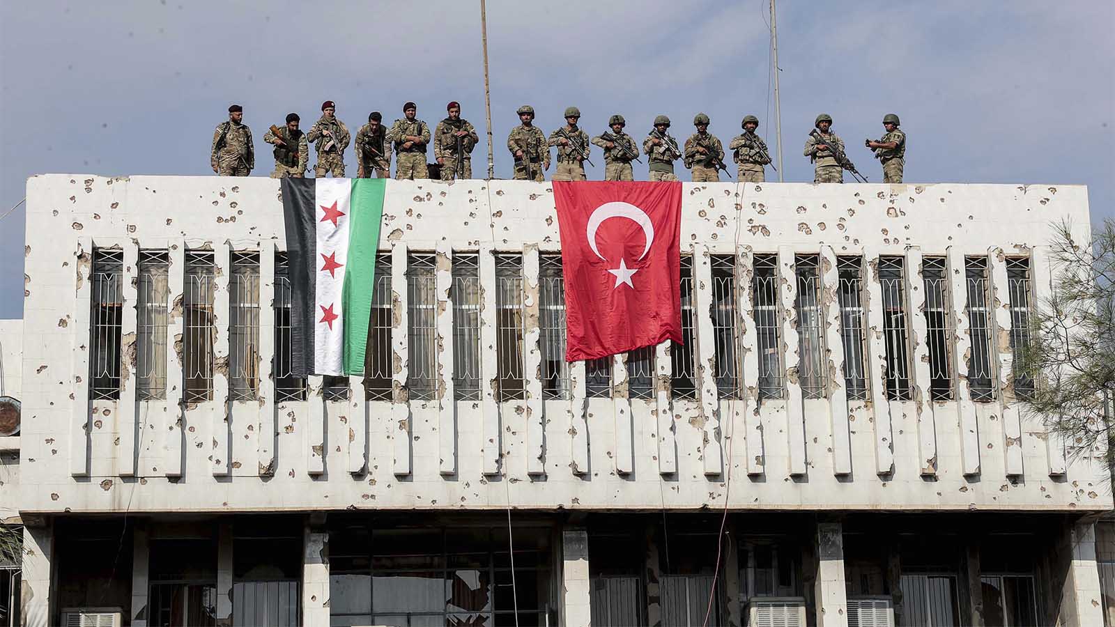 Turkish soldiers, right, and Turkey-backed opposition fighters stand atop a building next to their flags in Syrian town of Ras al Ayn, northeastern Syria, Wednesday, Oct. 23, 2019. Turkish media reports say Turkish troops and their allied Syrian opposition forces are securing a town in northeast Syria after Syrian Kurdish fighters pulled out of the area.(Ugur Can/DHA via AP)