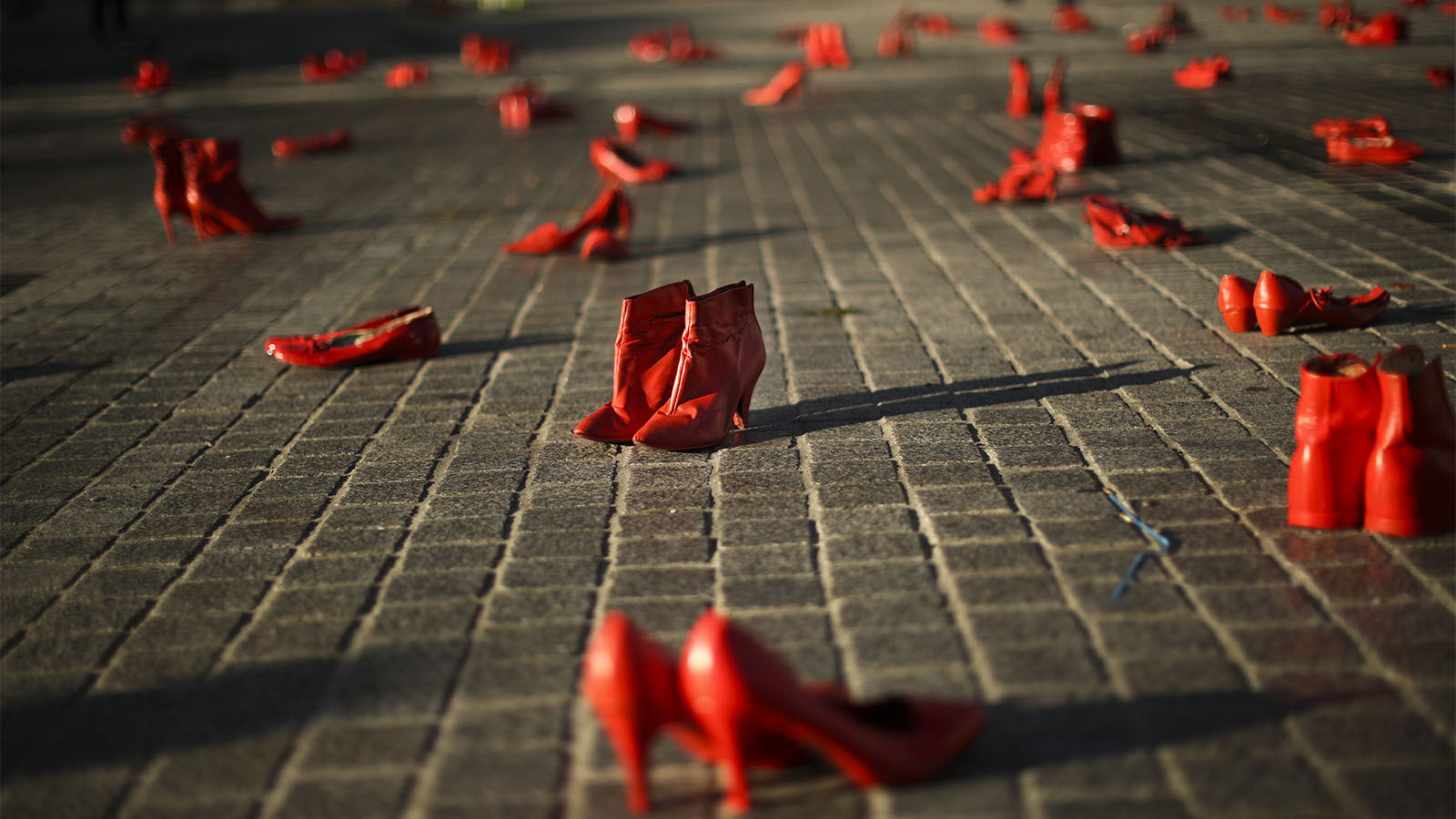 עוברי אורח צועדים ליד עשרות נעלי נשים צבועות באדום המונחות על המדרכה כחלק ממיצג המיועד לעורר מודעות לאלימות המופנית כנגד נשים. בריסל. (AP Photo/Francisco Seco)