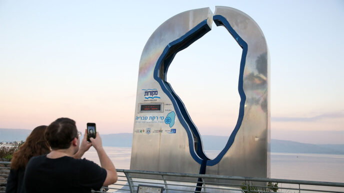 Visitors standing near a sign displaying the Kinneret water level on the beach promenade of the Northern Israeli city of Tiberias, right by the Kinneret lake on March 18, 2019. (Photograph: David Cohen/Flash90)