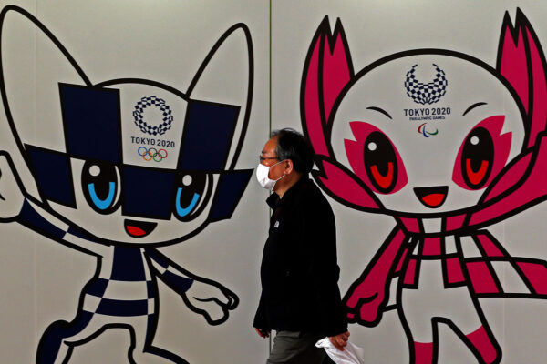 איש יפני עם מסיכה על רקע סמלי המשחקים האולימפיים והפראלימפיים בטוקיו 2020 
(by Buddhika Weerasinghe/Getty Images)