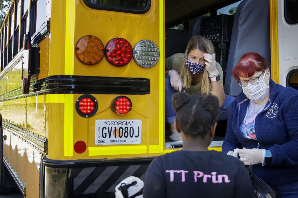 מורות מחלקות ארוחות  מתוך אוטובוס בית-ספרי בג'ורג'יה שבארה"ב. המגפה מנעה מתלמידים רבים לקבל את הארוחה המונפקת להם על ידי המדינה באמצעות בית הספר שלהם. מאי 2020. (AP Photo/Brynn Anderson)