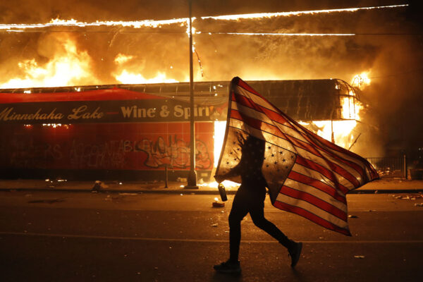 מפגין עם דגל ארה"ב סמוך לבניין המשטרה שהוצת במינאפוליס, מינסוטה במחאה על מותו של ג'ורג' פלויד. (AP Photo/Julio Cortez)