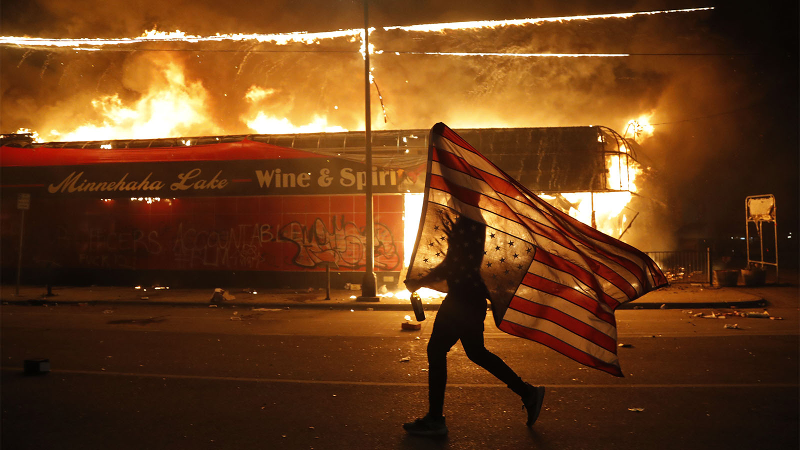 מפגין עם דגל ארה&quot;ב סמוך לבניין המשטרה שהוצת במינאפוליס, מינסוטה במחאה על מותו של ג'ורג' פלויד. (AP Photo/Julio Cortez)