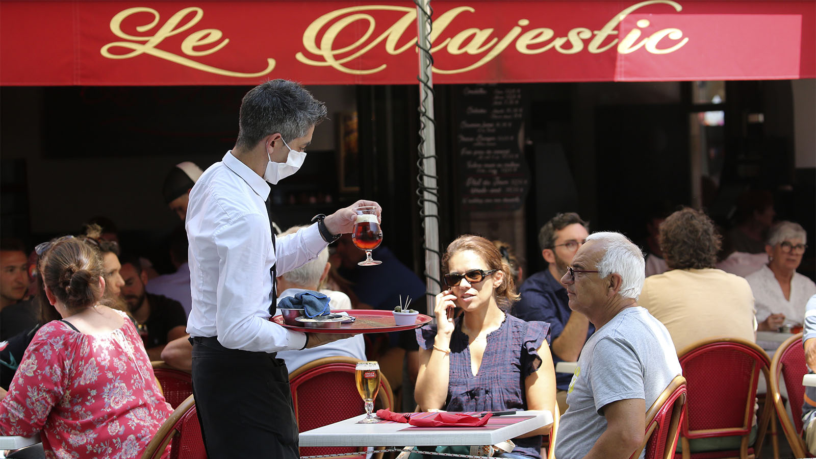 מלצר מביא משקאות לשולחן ללקוחות בבית הקפה בסן ז'אן דה לוז שבדרום מערב צרפת (AP Photo/Bob Edme)
