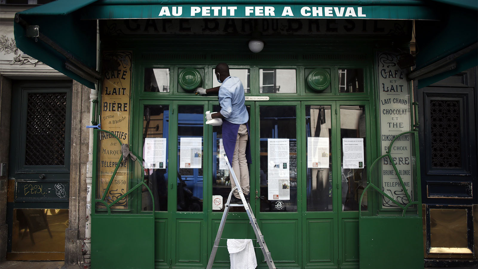 ג'יבריל, עבוד באחד מבתי הקפה בפריז, מנקה את החלון הקדמי של בית הקפה הסגור (AP Photo/Thibault Camus)