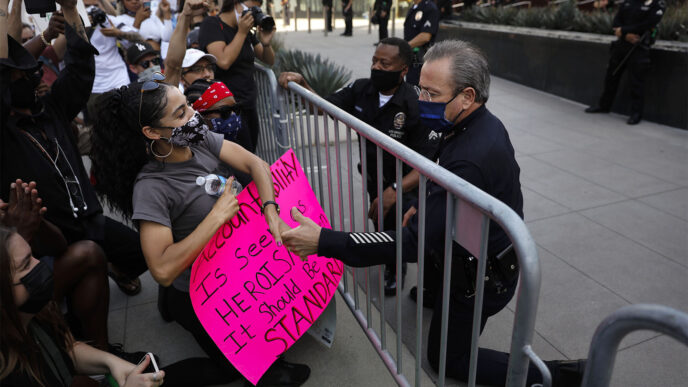 שוטר בלוס אנג'לס כורע ברך ומושיט יד למפגינה כאות הזדהות, בזמן הפגנה בעקבות הרצח של ג'ורג' פלויד (צילום: AP Photo/Jae C. Hong).