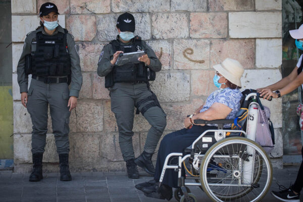 אישה מבוגרת והמטפלת שלה חולפות על פני שוטרות מג"ב בירושלים. יולי 2020 (צילום: יונתן זינדל/פלאש90)