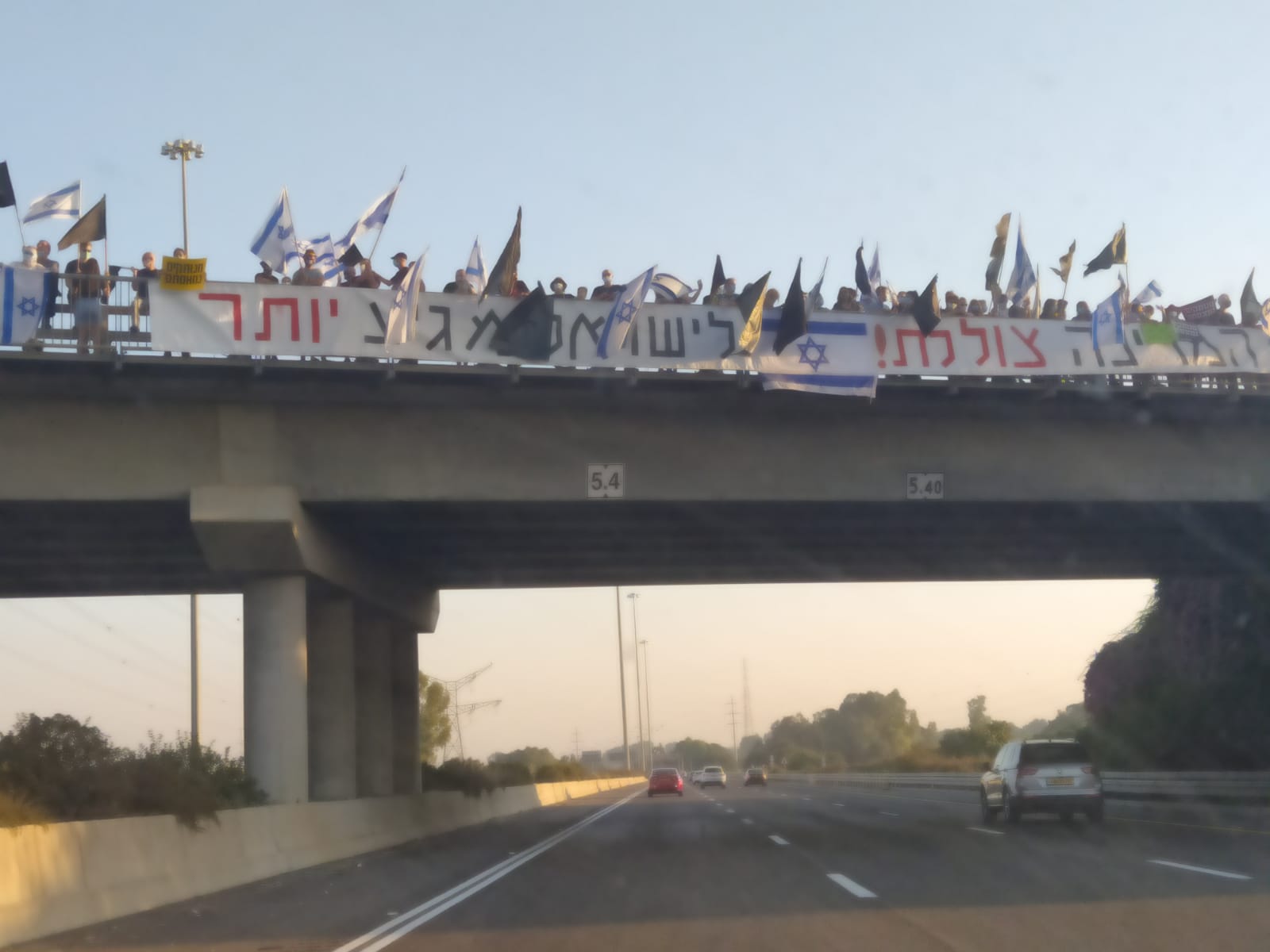 Demonstrators waving black flags and flags of Israel on top a bridge above Route 6 highway. (photo: Elad Madan)
