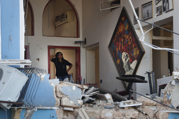 אישה עומדת בפתח מסעדה באיזור הנמל שנהרסה מהדף הפיצוץ (צילום: AP Photo/Hussein Malla).
