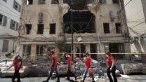 סטודנטים שהתנדבו לסייע בניקיון ההריסות חולפים על פני בניין שנפגע בפיצוץ בנמל ביירות. (צילום: AP Photo/Hussein Malla)