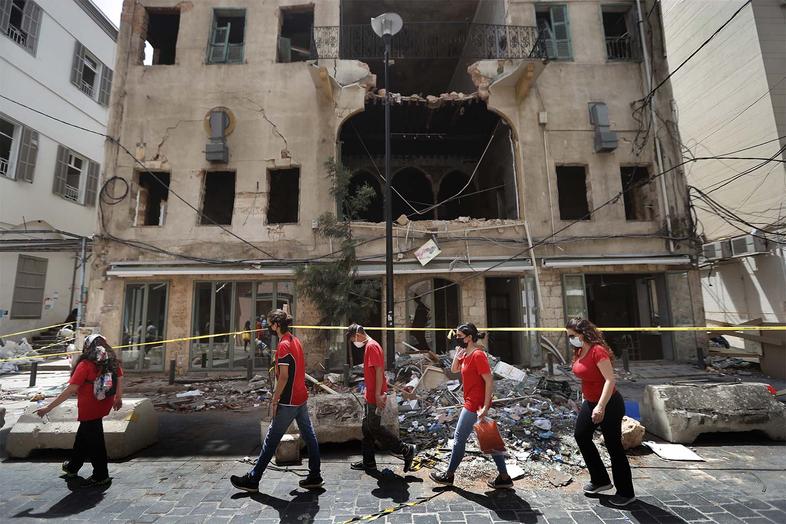 סטודנטים שהתנדבו לסייע בניקיון ההריסות חולפים על פני בניין שנפגע בפיצוץ בנמל ביירות. (צילום: AP Photo/Hussein Malla)