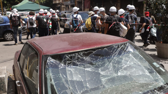 צעירים לבנונים שהתגייסו לסייע בניקיון הבתים שנפגעו בפיצוץ בנמל ביירות חולפים על פני מכונית שנפגעה מההדף. (צילום: (AP Photo/Hussein Malla
