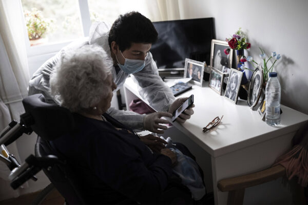 עובד סיעוד מסייע לקשישה להתקשר אל קרוביה במהלך מגפת הקורונה. מדריד, ספרד, אפריל 2020 (צילום: AP Photo/Bernat Armangue)