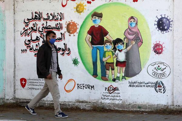 צעיר עזתי ליד ציור קיר המזהיר מפני נגיף הקורונה (צילום: Abed Rahim Khatib/פלאש90)