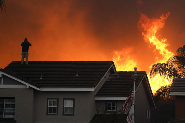 אדם עומד על גג ביתו כאשר האש של "בלו רידג'" בוערת על צלע הגבעה ב-27 באוקטובר 2020, בצ'ינו הילס, קליפורניה (צילום: AP/Jae C. Hong)