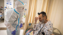 מתנדב בבית החולים מסייע לחולה לחבוש את התפילין (צילום: אוליבר פיטוסי, פלאש 90)